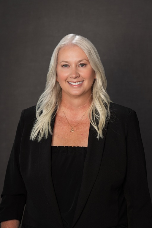 Professional headshot of a person wearing a black blazer and black top against a dark studio background.