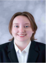 Professional headshot of a person with short, light-brown hair, wearing a dark blazer over a white collared shirt. The person is facing the camera. The portrait is cropped from the shoulders up and set against a softly blurred light gray patterned background.