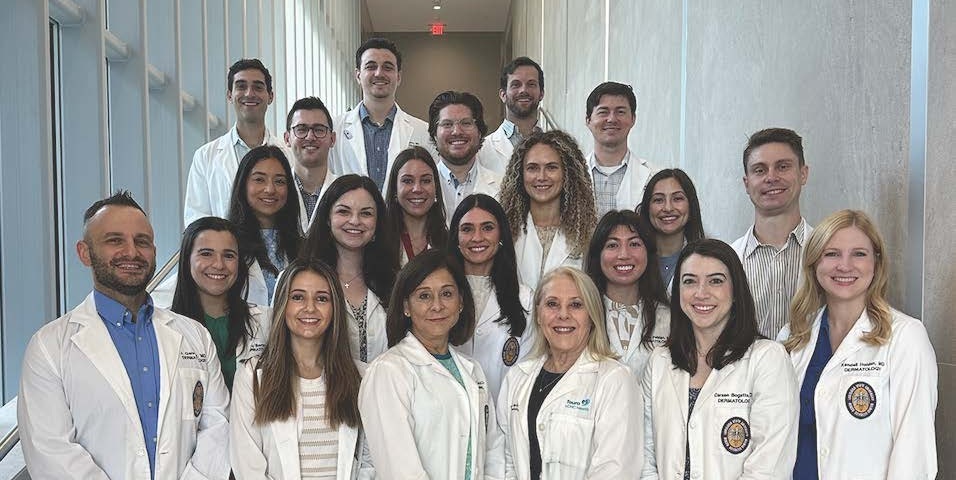 Group of professionals wearing white lab coats standing together in a well-lit hallway, arranged in three rows and facing the camera.