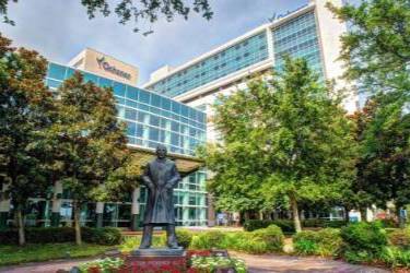 Exterior of Ochsner Medical Center with a statue in the foreground surrounded by trees and landscaped grounds.