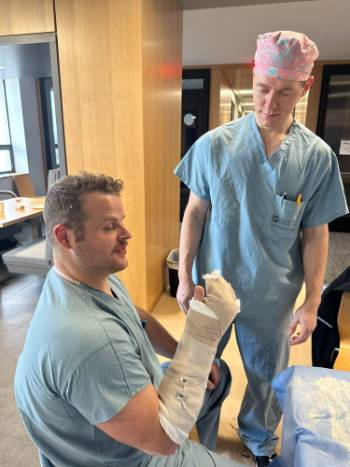 Doctor in scrubs wearing splint while other doctor looks on